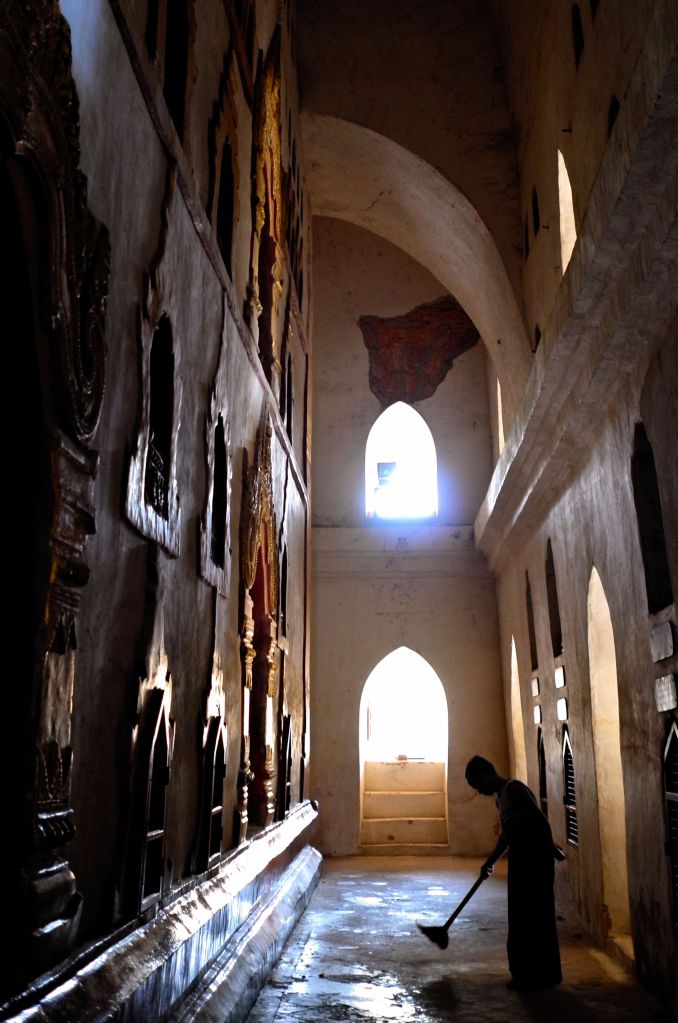 Caretaker of Ananda temple (Bagan, Myanmar) sweeping the inside of the template with wall niches at sunset